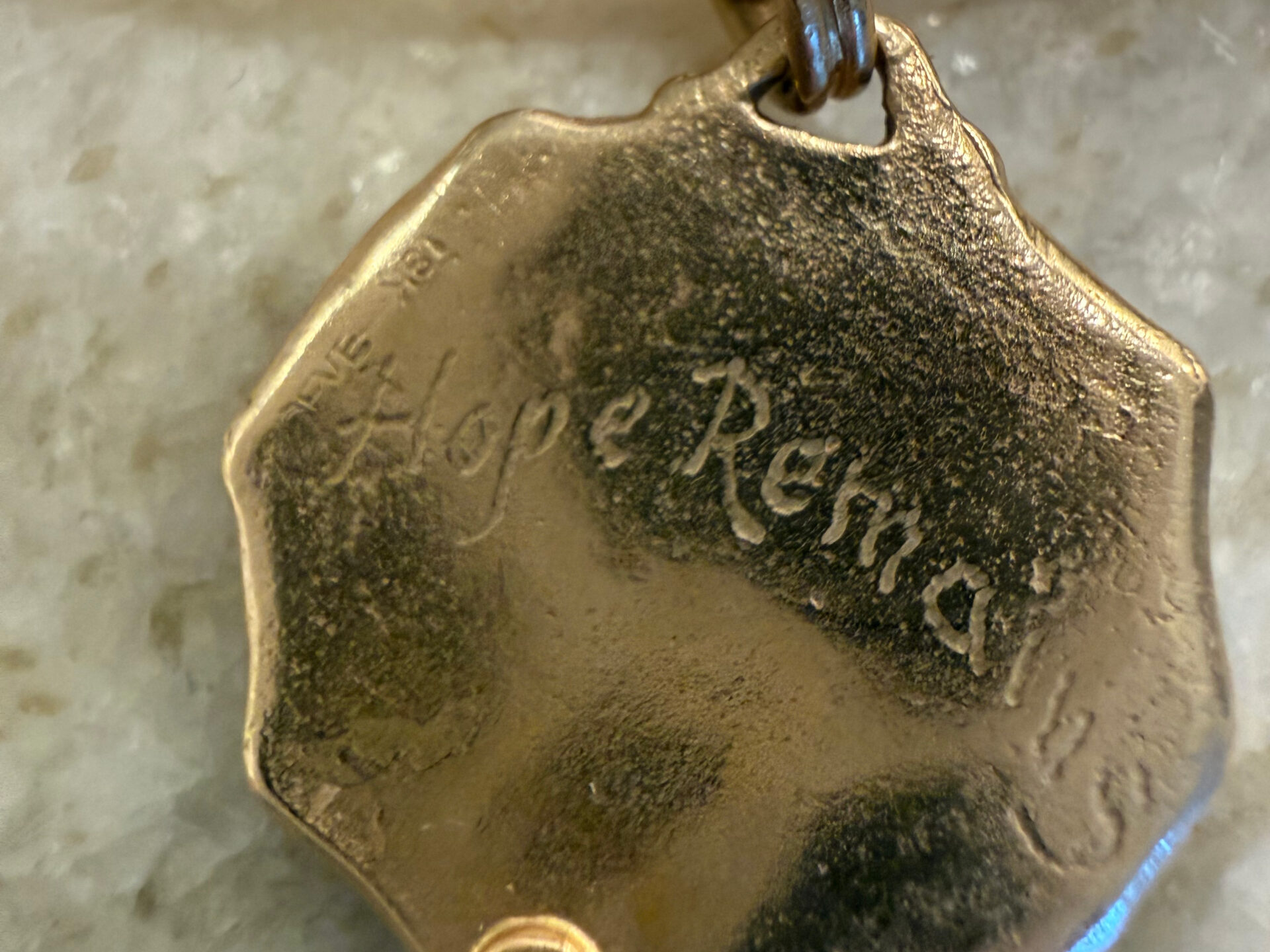 Gold pendant engraved “Hope Remains” with a small red stone.