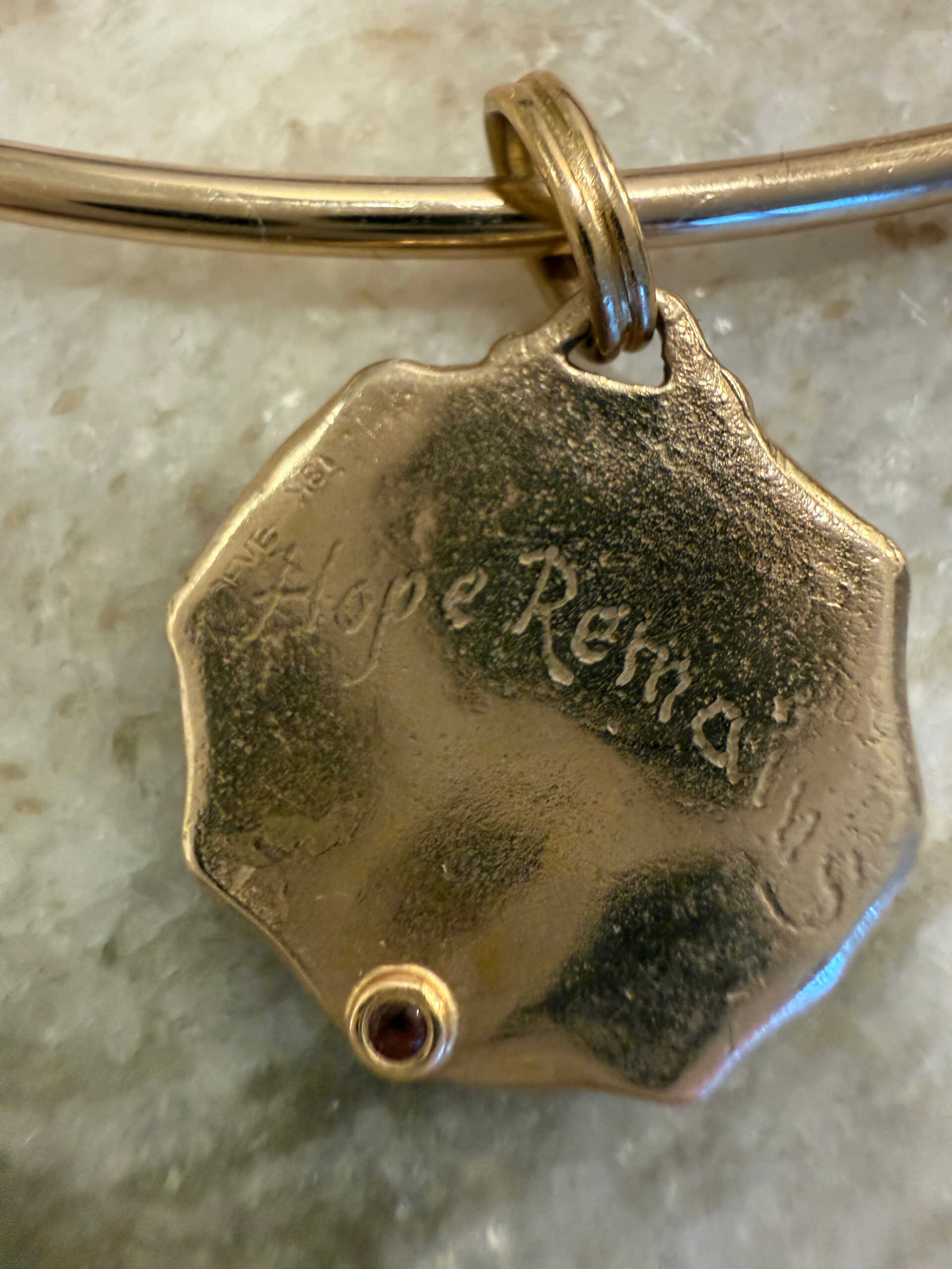 Gold pendant engraved “Hope Remains” with a small red stone.