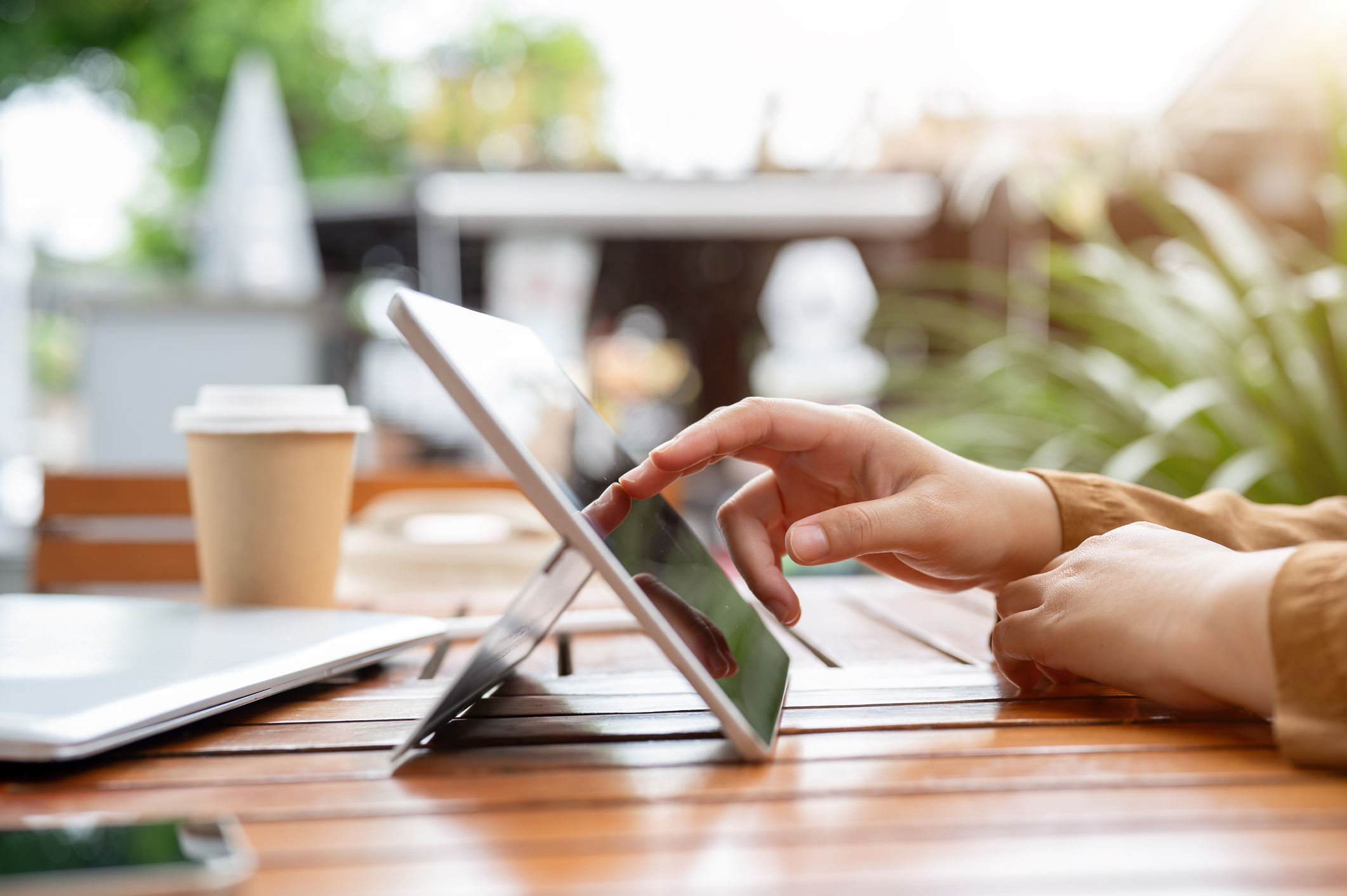 Tools and Resources hero A person using a tablet at a sunlit outdoor cafe table, coffee cup nearby